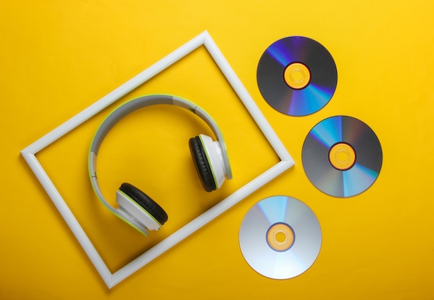 Fones de ouvido estéreo elegantes e discos de CD na superfície amarela com moldura branca