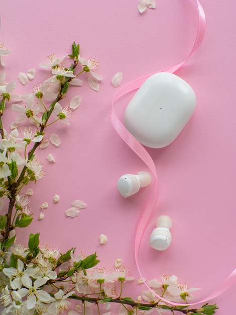 Fones de ouvido sem fio em fundo rosa com flores de cerejeira e espaço para texto