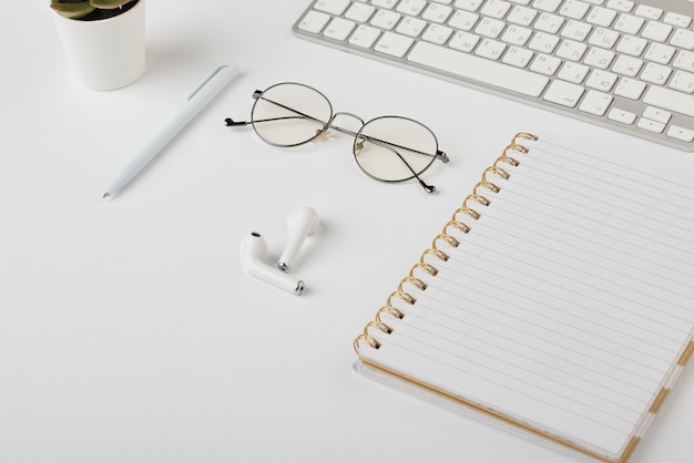 Fones de ouvido sem fio, óculos, caneta, notebook e teclado de computador na mesa branca que é o local de trabalho do gerente de escritório