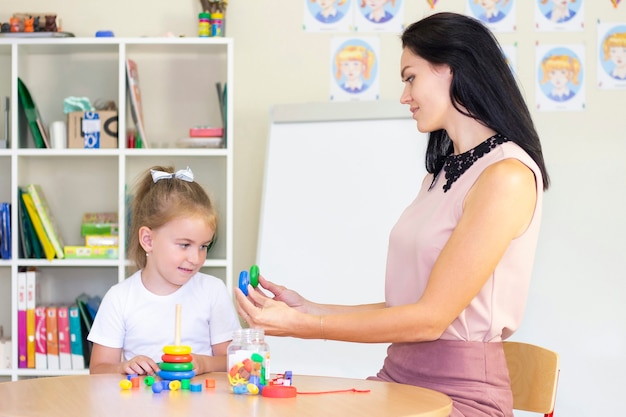 Foto fonoaudiólogo ensina uma garota. coletar pirâmide infantil, desenvolvimento infantil, habilidades motoras finas