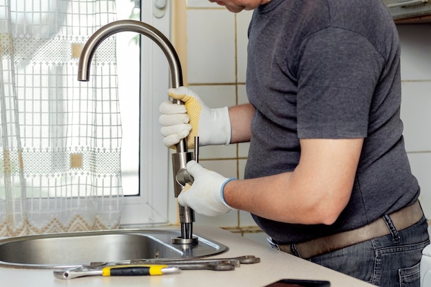 Un fontanero en la cocina instala un nuevo grifo de agua. Reparación del grifo de la cocina cerca del fregadero.