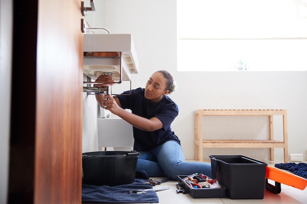 Fontanero femenino trabajando para arreglar fregadero con fugas en el baño de la casa