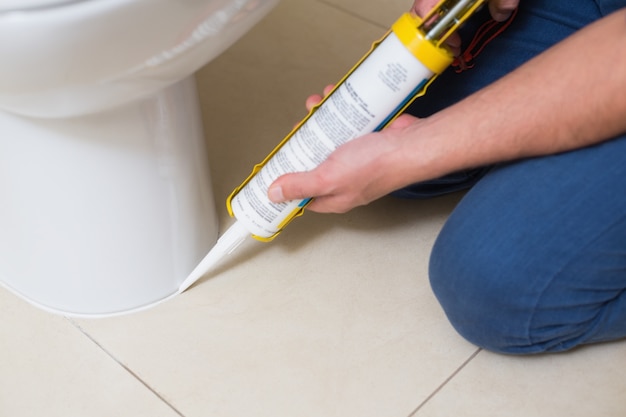 Fontanero fijación inodoro en un baño con cartucho de silicona