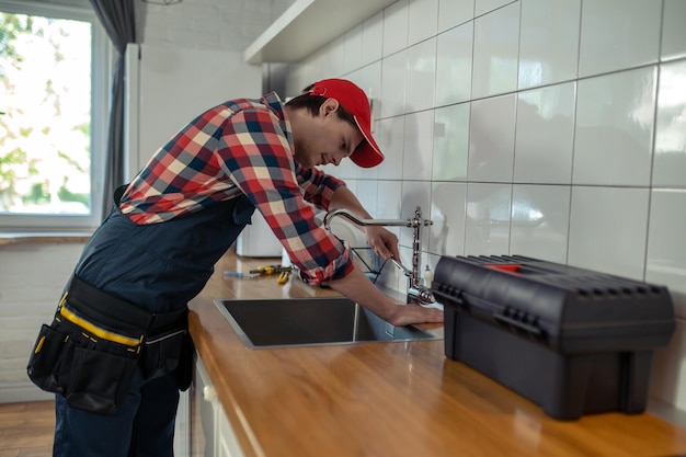 Fontanero joven serio que repara un grifo de cocina