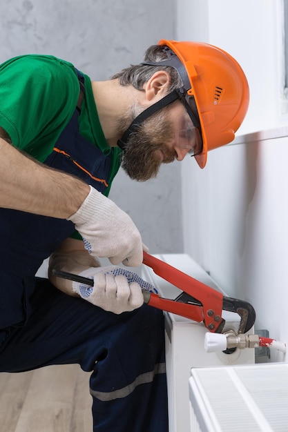 Foto un fontanero macho instala un radiador en el sistema de calefacción de un apartamento guy en overoles y una llave de gas