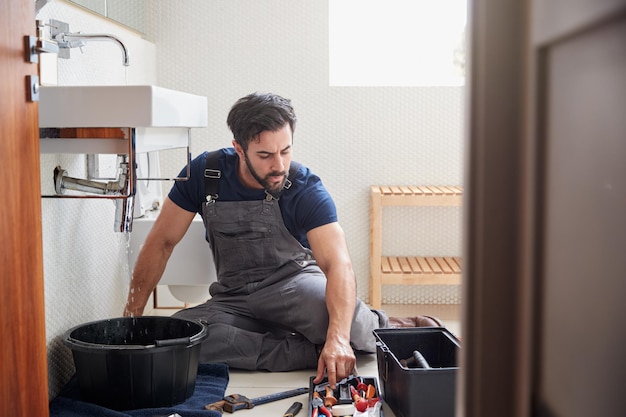Fontanero masculino trabajando para arreglar el fregadero con fugas en el baño de la casa