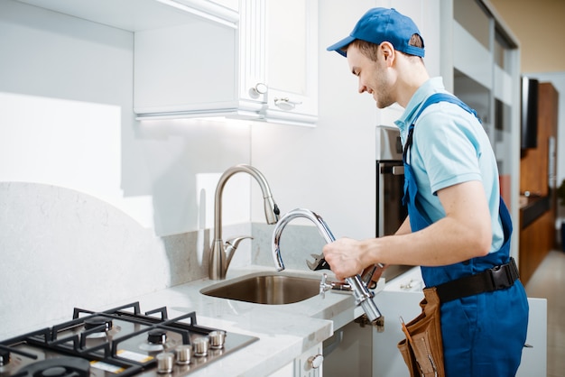 Fontanero masculino en uniforme cambia de grifo en la cocina. Manitas con fregadero de reparación de bolsa de herramientas, servicio de equipamiento sanitario a domicilio