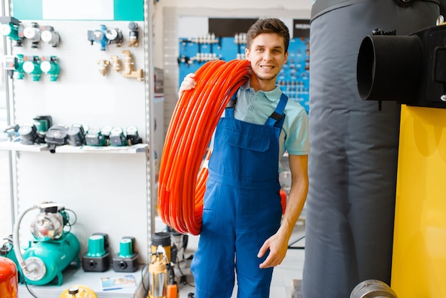 Fontanero en uniforme tiene rollo de tubería en la tienda de fontanería. Hombre comprando ingeniería sanitaria en la tienda