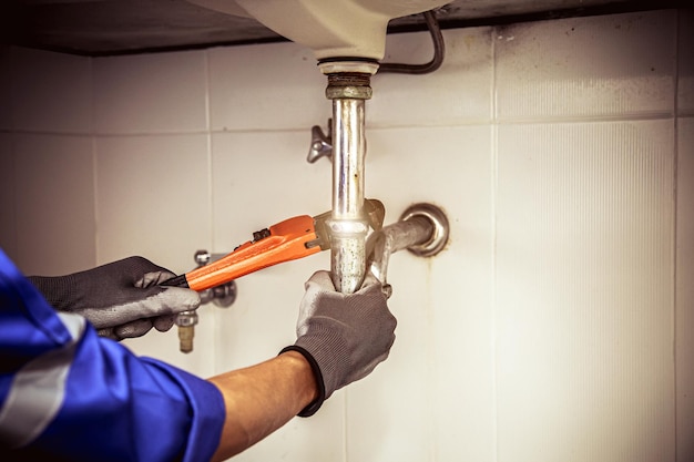 Fontanero usando una llave para reparar la tubería de agua debajo del fregadero