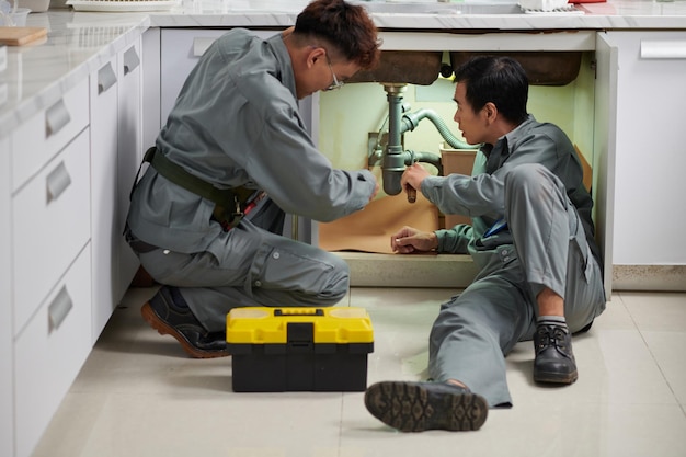 Fontaneros instalando nuevos tubos de plástico debajo del fregadero de la cocina