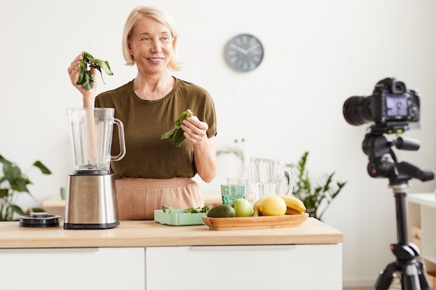 Food-Blogger lächelt in die Kamera und zeigt den Prozess der Herstellung eines gesunden Cocktails in der Küche