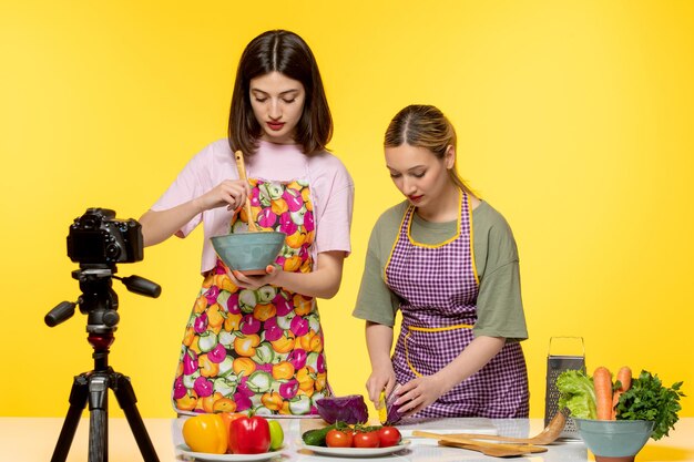 Food Blogger süßer, reizender Koch in rosa Schürze mit einem Freund, der einen Salat macht