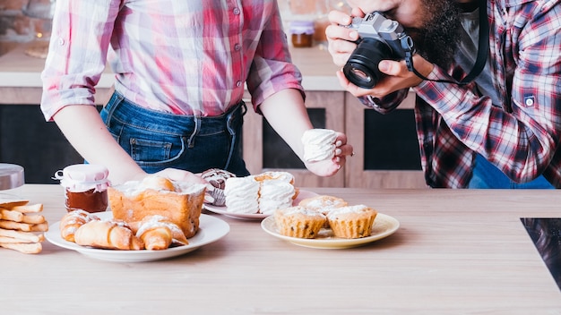 Food-Fotograf und Assistent bei der Arbeit. Mann und Frau, die Baiser fotografieren. Kuchen- und Gebäcksortiment rund um.