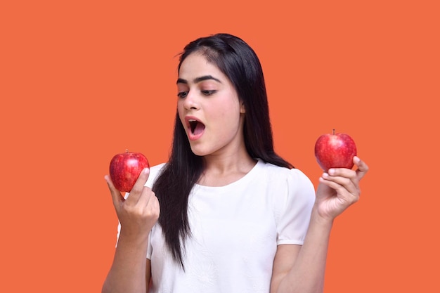 foodie chica con camiseta blanca comiendo manzana sobre fondo naranja modelo paquistaní indio