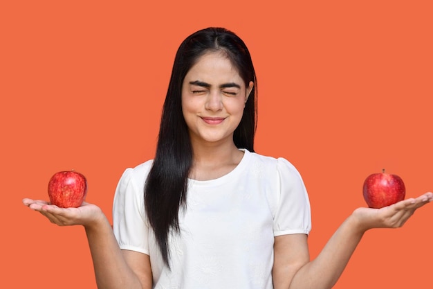 foodie chica con camiseta blanca sosteniendo dos manzanas con los ojos cerrados modelo paquistaní indio