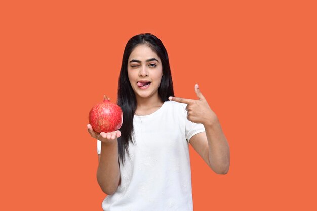 foodie chica con camiseta blanca sosteniendo granada y lame sus labios modelo paquistaní indio