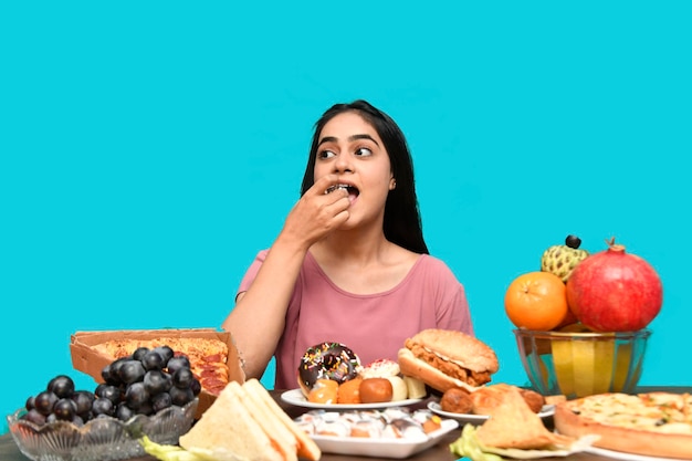 foodie chica sentada en la mesa de frutas comiendo cupcake mirando a la izquierda modelo paquistaní indio
