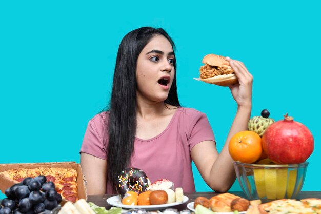 foodie chica sentada en la mesa de frutas sosteniendo una hamburguesa modelo paquistaní indio