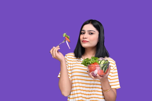 Foto foodie chica sosteniendo una cuchara y un tazón de ensalada posando sobre fondo púrpura modelo paquistaní indio