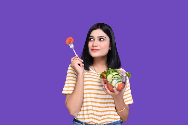 Foodie chica sujetando ensaladera de verduras sobre fondo morado modelo paquistaní indain