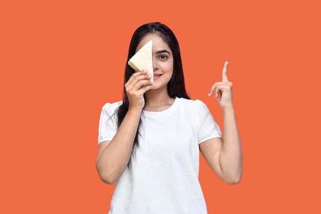 Foodie chica vestida con camiseta blanca sonriendo y esconde su rostro con sándwich modelo paquistaní indio