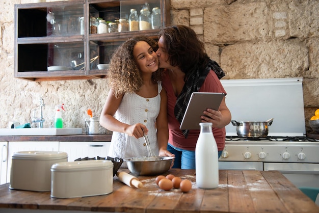 Foodie feminino curvilíneo cozinhando com sua filha enquanto olha sua receita on-line em um tablet