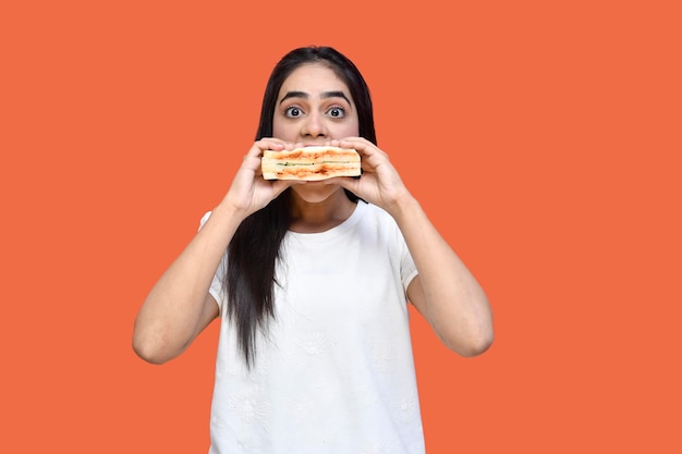 Foto foodie garota vestindo camiseta branca comendo sanduíche sobre fundo laranja modelo indiano do paquistanês