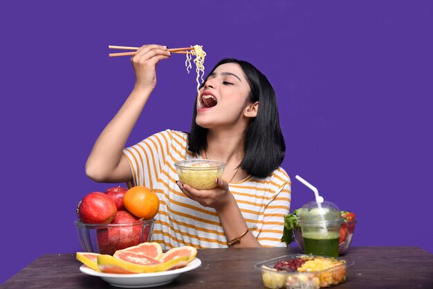 foodie girl sentada à mesa de frutas comendo macarrão modelo indiano do paquistanês