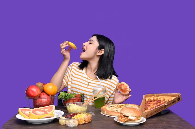 Foto foodie girl sentada à mesa de frutas e comendo frutas cítricas modelo indiano do paquistanês