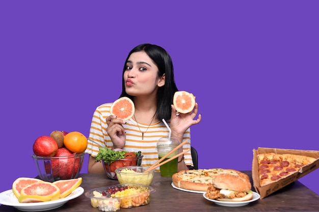 Foto foodie girl sentada à mesa de frutas segurando frutas cítricas e soprando um beijo modelo indiano do paquistanês