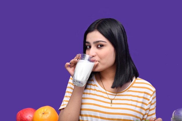 foodie girl sentada na mesa de frutas bebendo leite sobre fundo roxo modelo indiano do paquistanês
