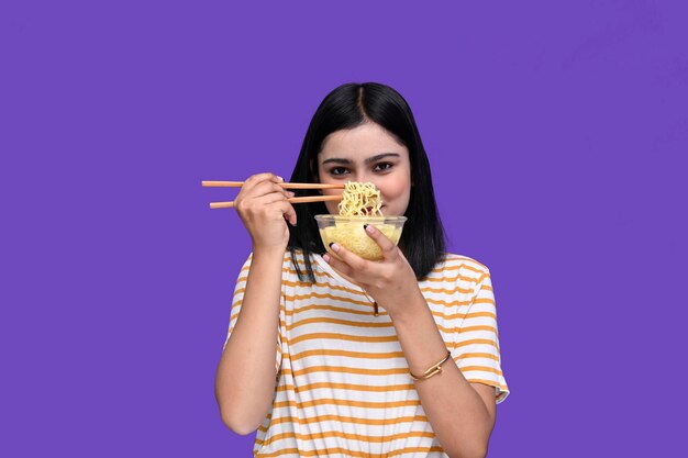 Foto foodie girl sonriendo y sosteniendo un tazón de fideos sobre fondo púrpura modelo paquistaní indio