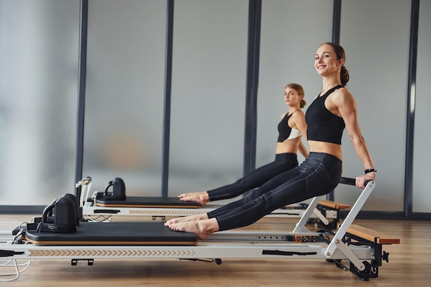 Força das mãos Duas mulheres em roupas esportivas e com corpos esbeltos têm dia de ioga fitness dentro de casa juntas