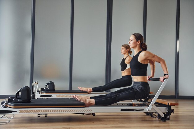 Força das mãos Duas mulheres em roupas esportivas e com corpos esbeltos têm dia de ioga fitness dentro de casa juntas