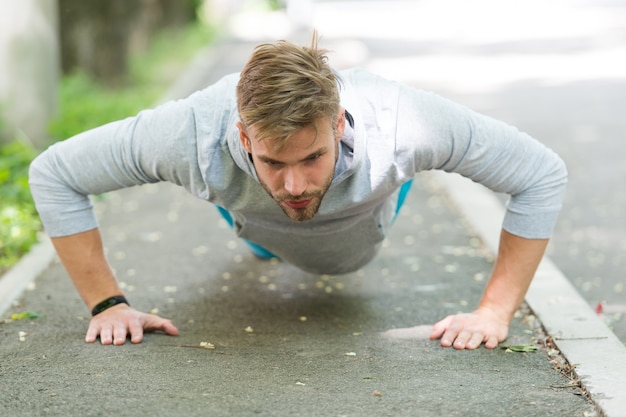 Força e motivação. Homem em roupas esportivas, fazendo flexões ao ar livre. Guy treino motivado no parque. O desportista melhora a sua força com exercícios de flexão. O homem tem motivação para conquistas esportivas de sucesso.