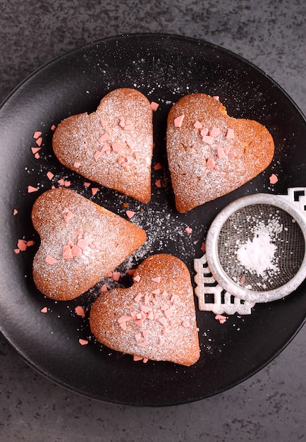 Fore cupcakes en el corazón con azúcar en polvo en un plato negro. Día de San Valentín.