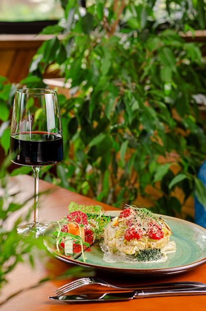 Forellenfilet mit Tomaten, Kirsche und Käse, serviert mit Gemüse und Rotwein. Mediterranes Mittagskonzept