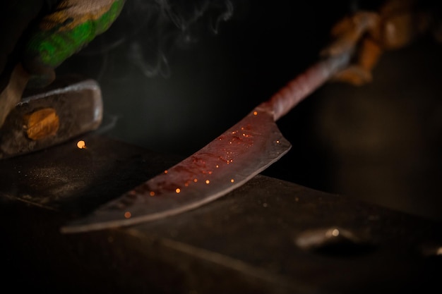 Forjando un cuchillo del metal en el taller oscuro