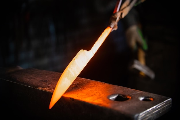 Forjando uma faca de metal quente segurando a faca em fórceps