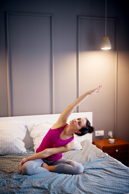 Forma atractiva deportiva mujer de mediana edad haciendo posturas de yoga sentado en la cama antes de dormir.