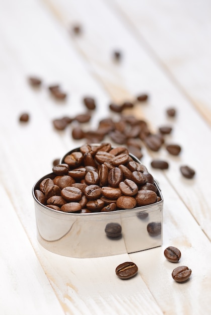 En forma de corazón de granos de café sobre la mesa de madera blanca