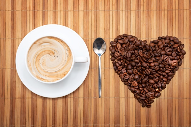 Foto en forma de corazón de granos de café con una taza de café sobre un fondo marrón