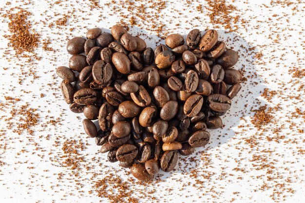 Forma de corazón de granos de café tostados marrones Café Robusta Arabica sobre un fondo de café molido sobre un fondo blanco