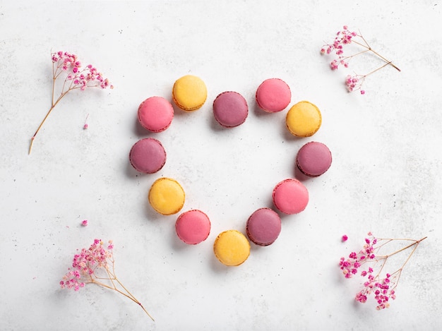 Forma de corazón hecha de macarons de colores. fondo blanco con marco de flores rosas