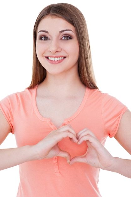 Forma de corazón. Hermosa mujer joven mirando a la cámara y haciendo forma de corazón con las manos mientras está de pie aislado en blanco