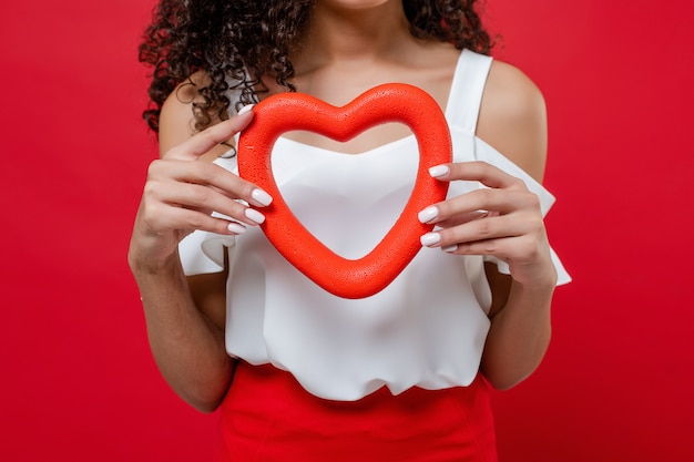 En forma de corazón en manos de mujer negra en blusa blanca aislada sobre rojo