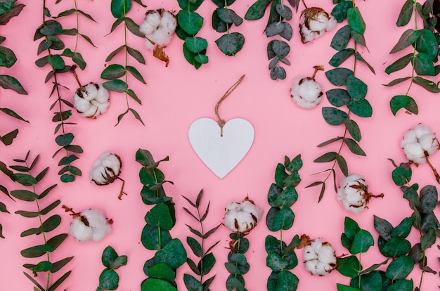 En forma de corazón con ramas de algodón y eucalipto sobre fondo rosa. Vista superior