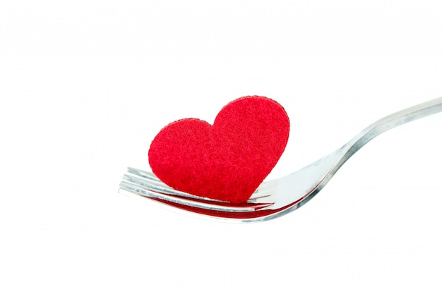 La forma de corazón rojo en un tenedor de plata, una cena romántica de amor o un concepto de salud para el cuidado del corazón