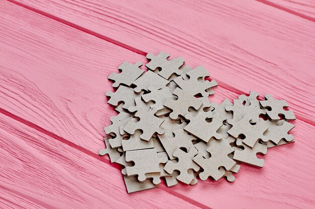 Foto forma de coração de papelão serra de vaivém. quebra-cabeças cinza jigzaw formando a forma de coração no fundo rosa de madeira. conceito de amor e romance.