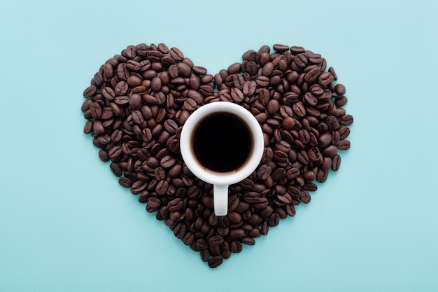 Forma de coração feita de grãos de café e uma xícara de café preto no azul